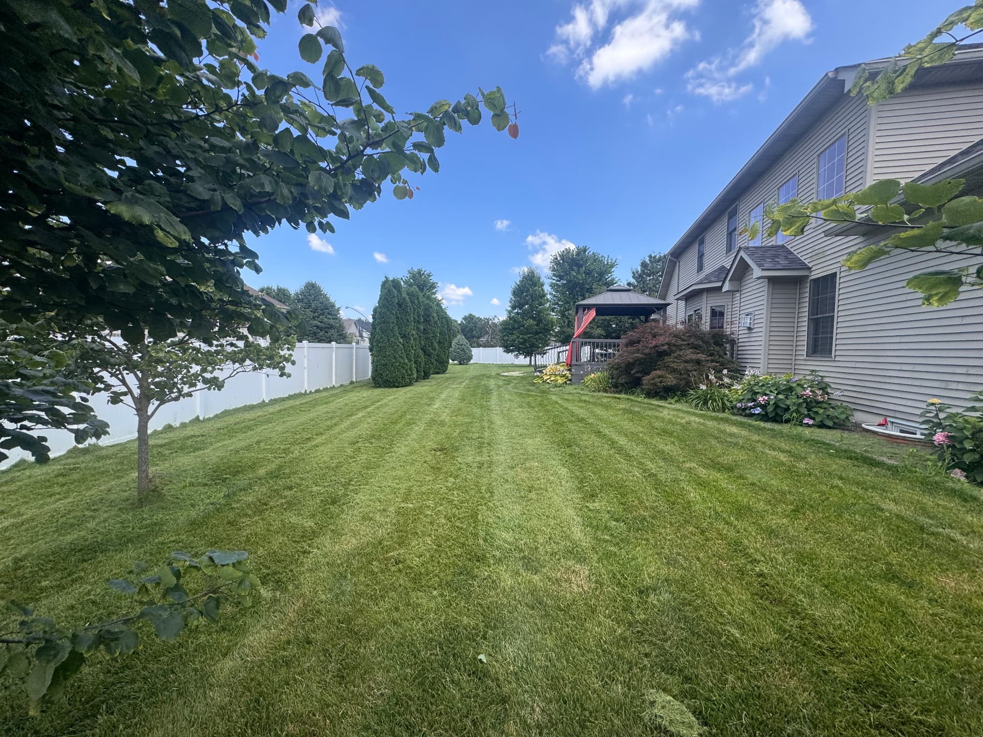 Side yard mowed in clean lines along a white privacy fence