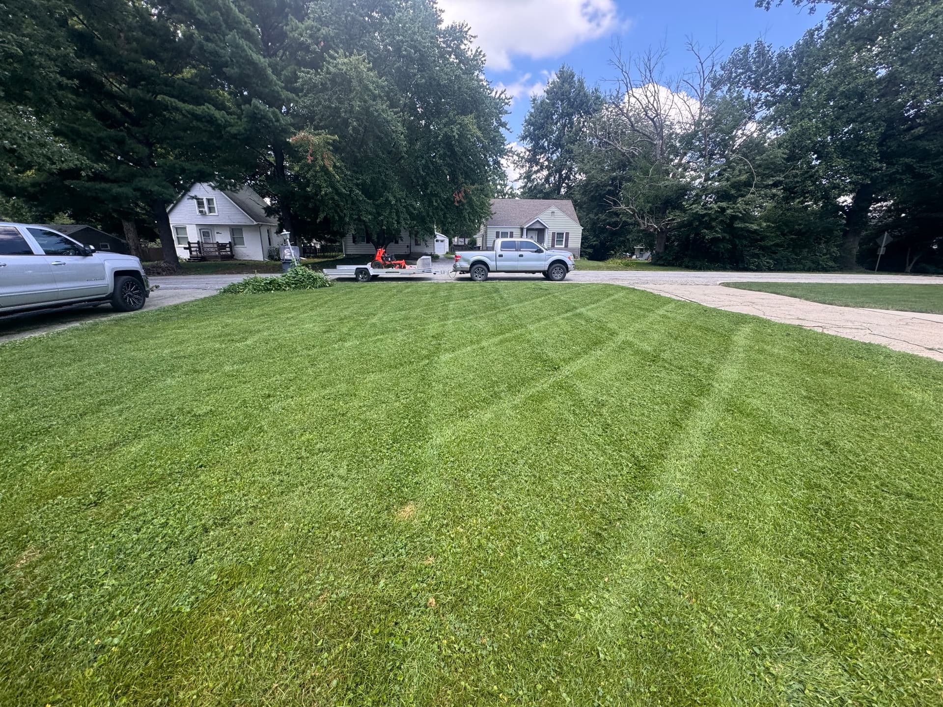 Freshly striped front yard with mower and trailer parked out front